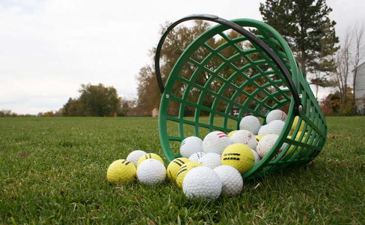 golf balls tipped over in bucket on green